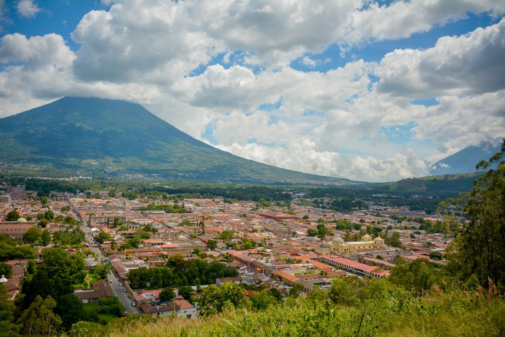 The low rooftops of Antigua Guatemala seen from a hillside, with the Agua volcano filling the horizon behind the town