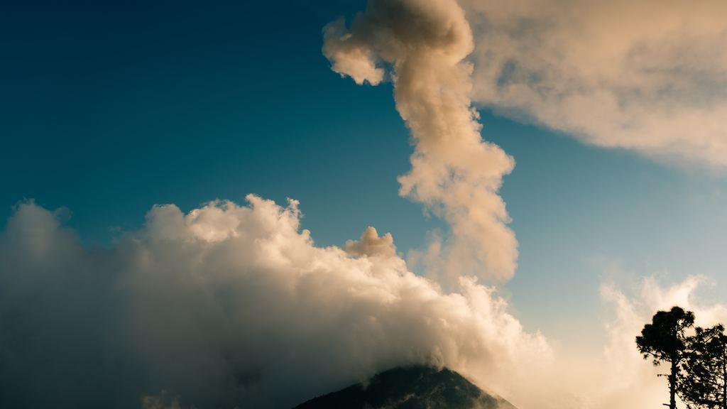 A tall ash column rising from the Fuego volcano at dusk, seen from the slopes of the Acatenango