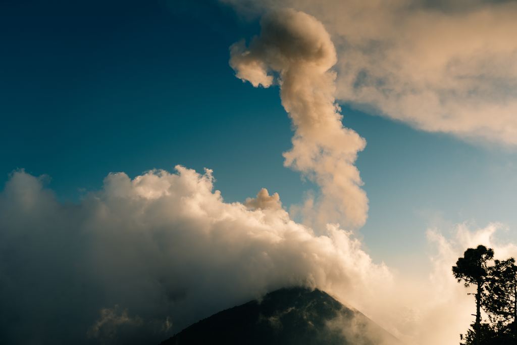 A tall ash column rising from the Fuego volcano at dusk, photographed from the slopes of the Acatenango in Guatemala