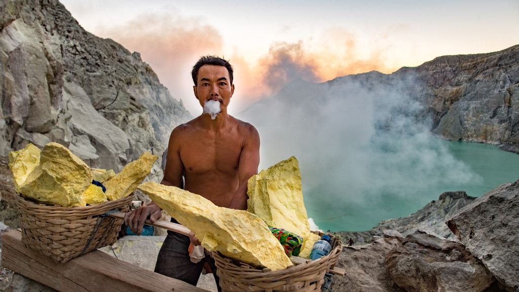Sulphur miners walking past blue flames of burning gas on the crater floor of Kawah Ijen at night