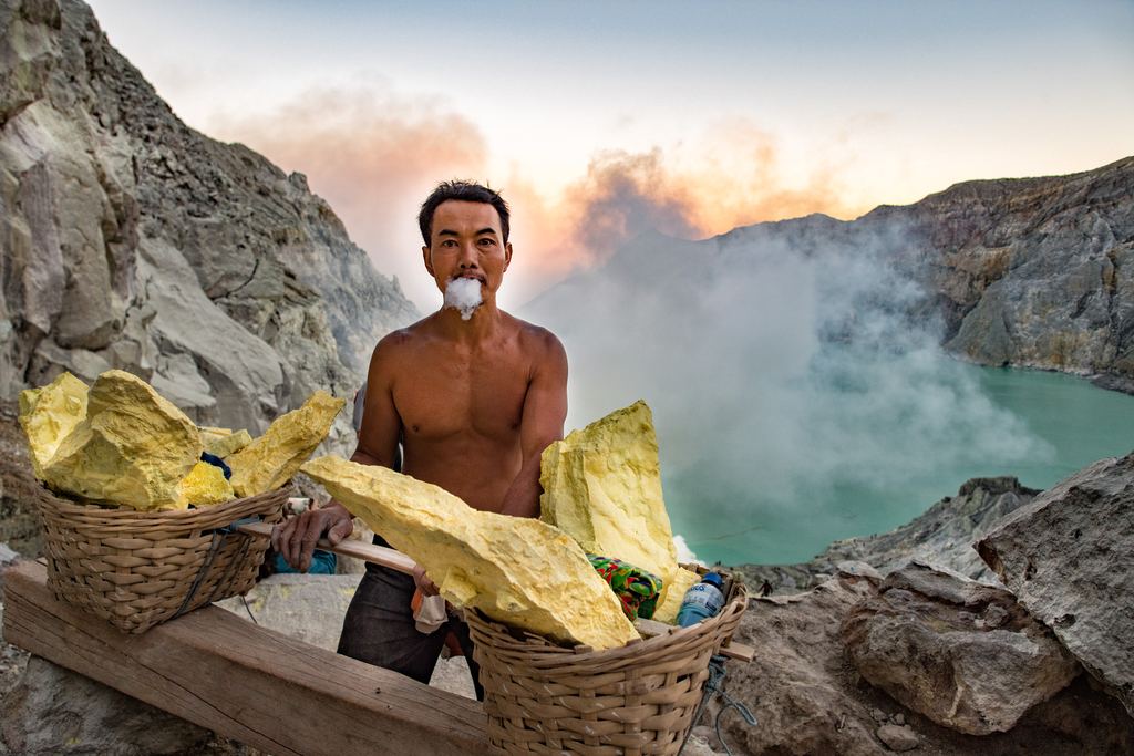 Sulphur miners walking past the blue flames on the crater floor of Kawah Ijen at night, East Java