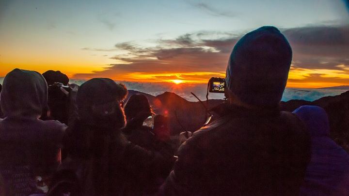 Bundled up travelers snap photos of the first rays of sun on Mount Haleakala in Maui's Haleakala National Park.