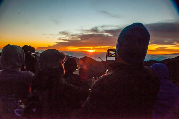 Bundled up travelers snap photos of the first rays of sun on Mount Haleakala in Maui's Haleakala National Park.