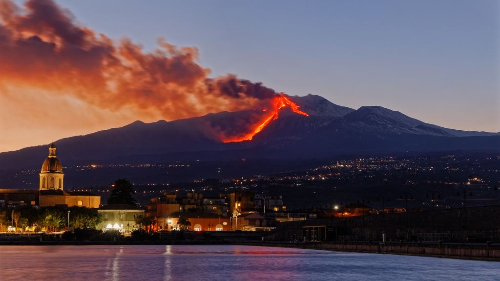 Mount Etna erupting at night above the lights of a Sicilian town