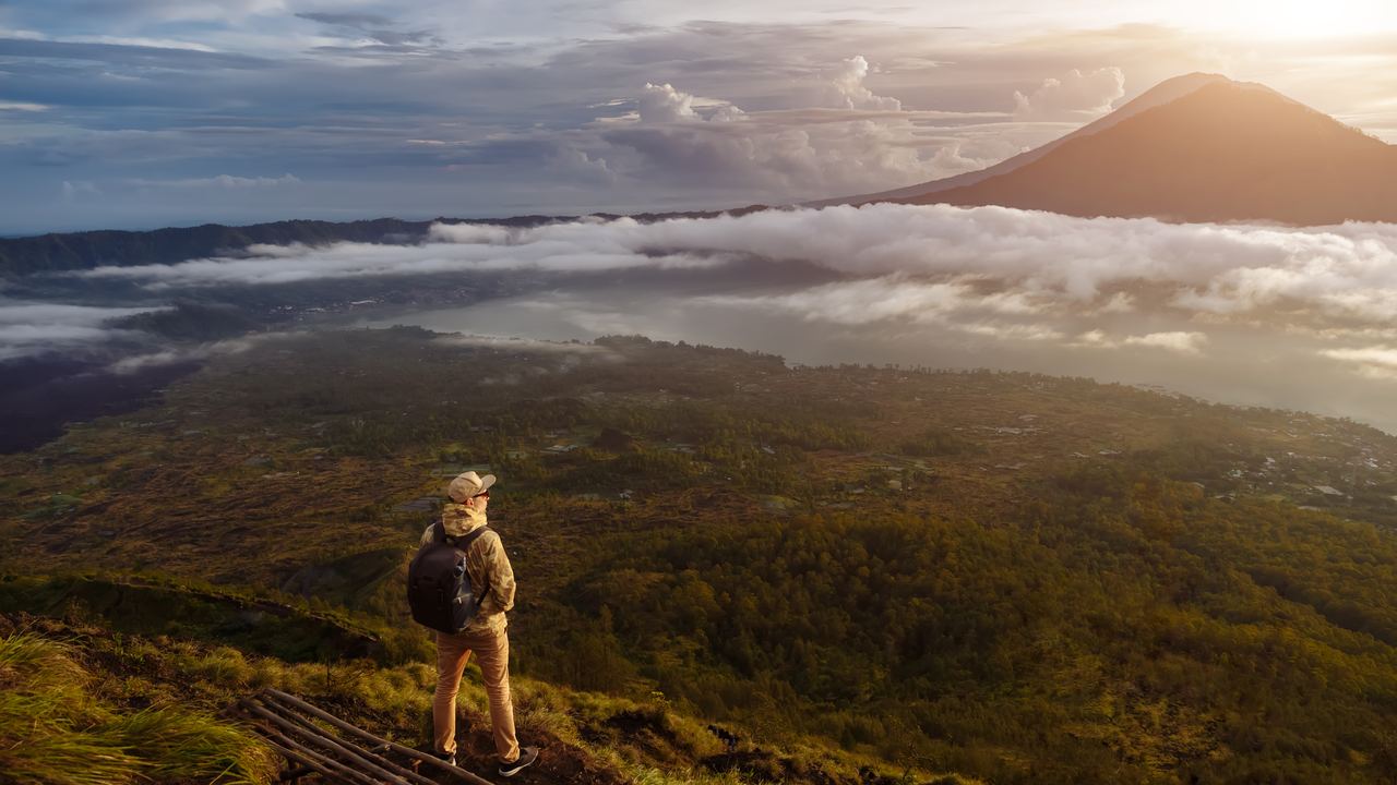 A trekker with a backpack watching the sunrise from the summit of Mount Batur, Bali, Indonesia