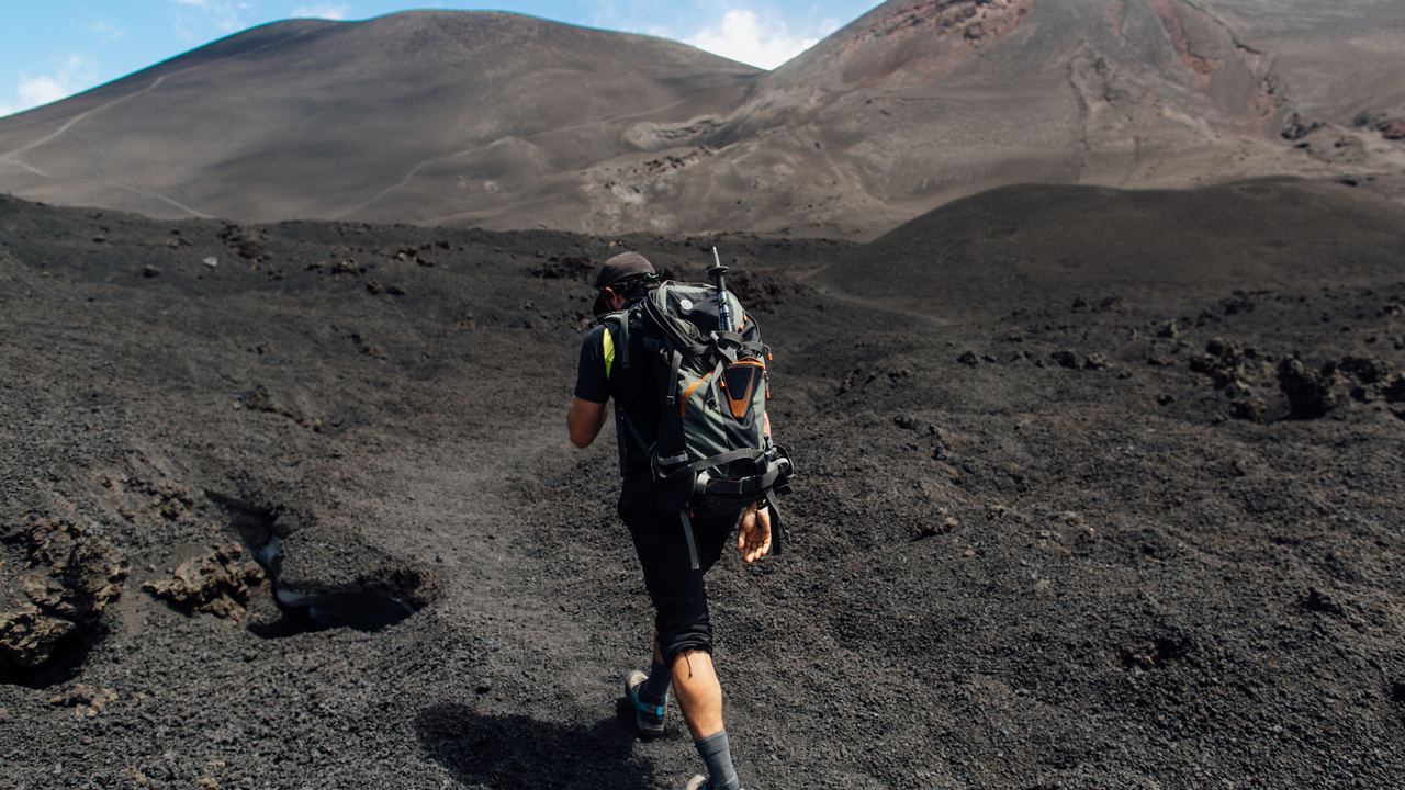 A hiker walking the loose volcanic gravel near a crater rim on Mount Etna, Sicily