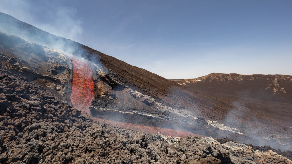 An incandescent lava channel running down Mount Etna into the Valle del Bove with gas rising from the flow