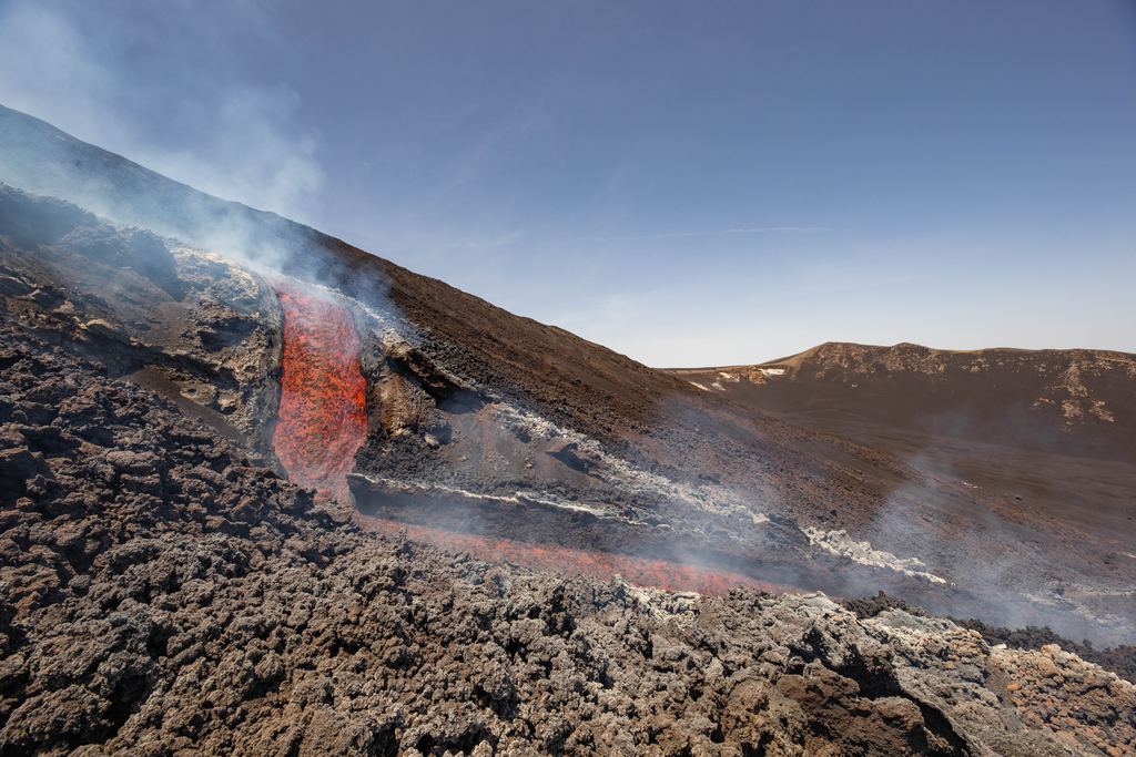 An incandescent lava channel running down Mount Etna into the Valle del Bove, with gas rising from the flow