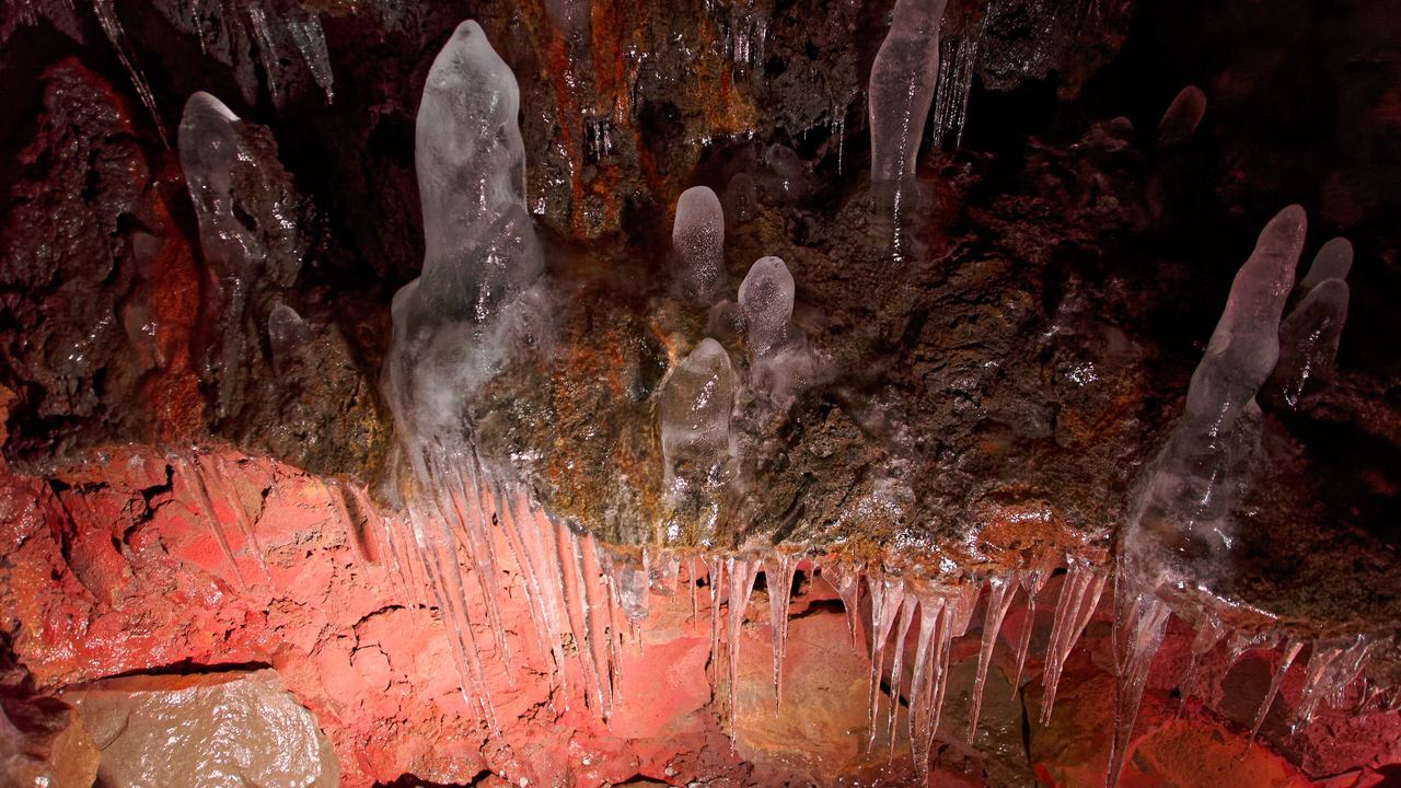 The lit interior of the Raufarhólshellir lava tube near Reykjavík, showing the coloured walls and the collapsed roof openings
