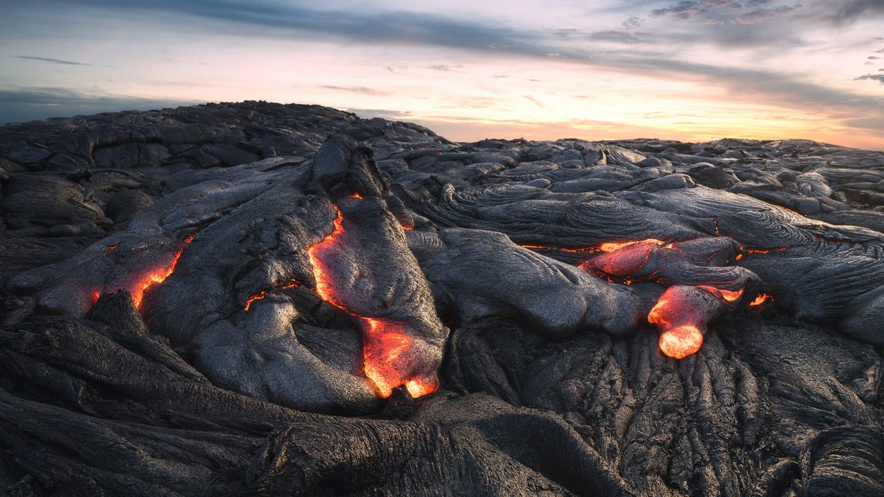 Molten lava glowing through the cracks of a cooled pahoehoe lava field at sunset