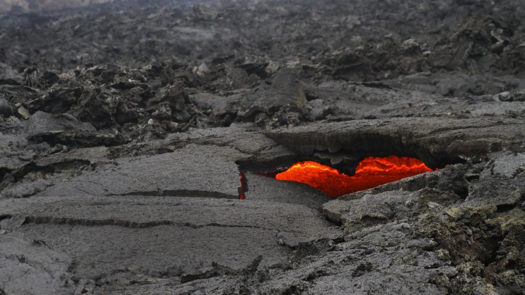 Glowing lava visible through a hole in the black hardened surface of a fresh lava field