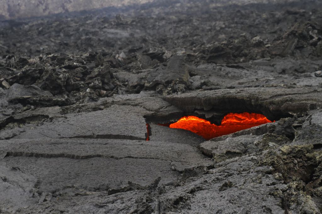 Molten lava glowing through an opening in the hardened black crust of a young lava field in Iceland