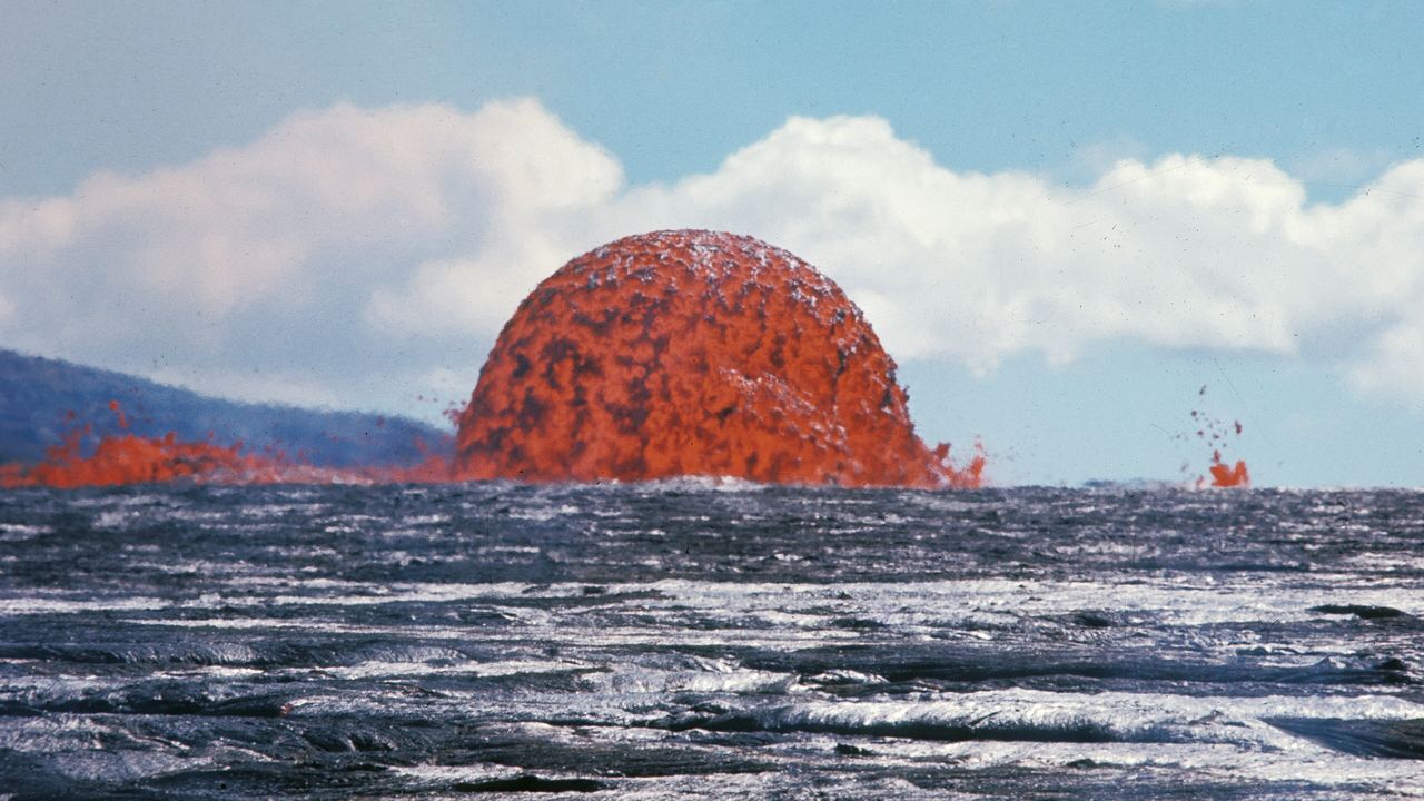Molten basaltic lava glowing orange-white as it fountains and spreads over dark cooled rock