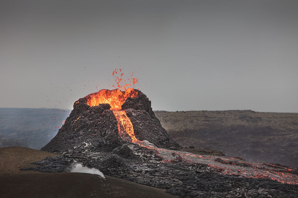 A tongue of molten lava moving downslope, glowing orange against dark cooled rock
