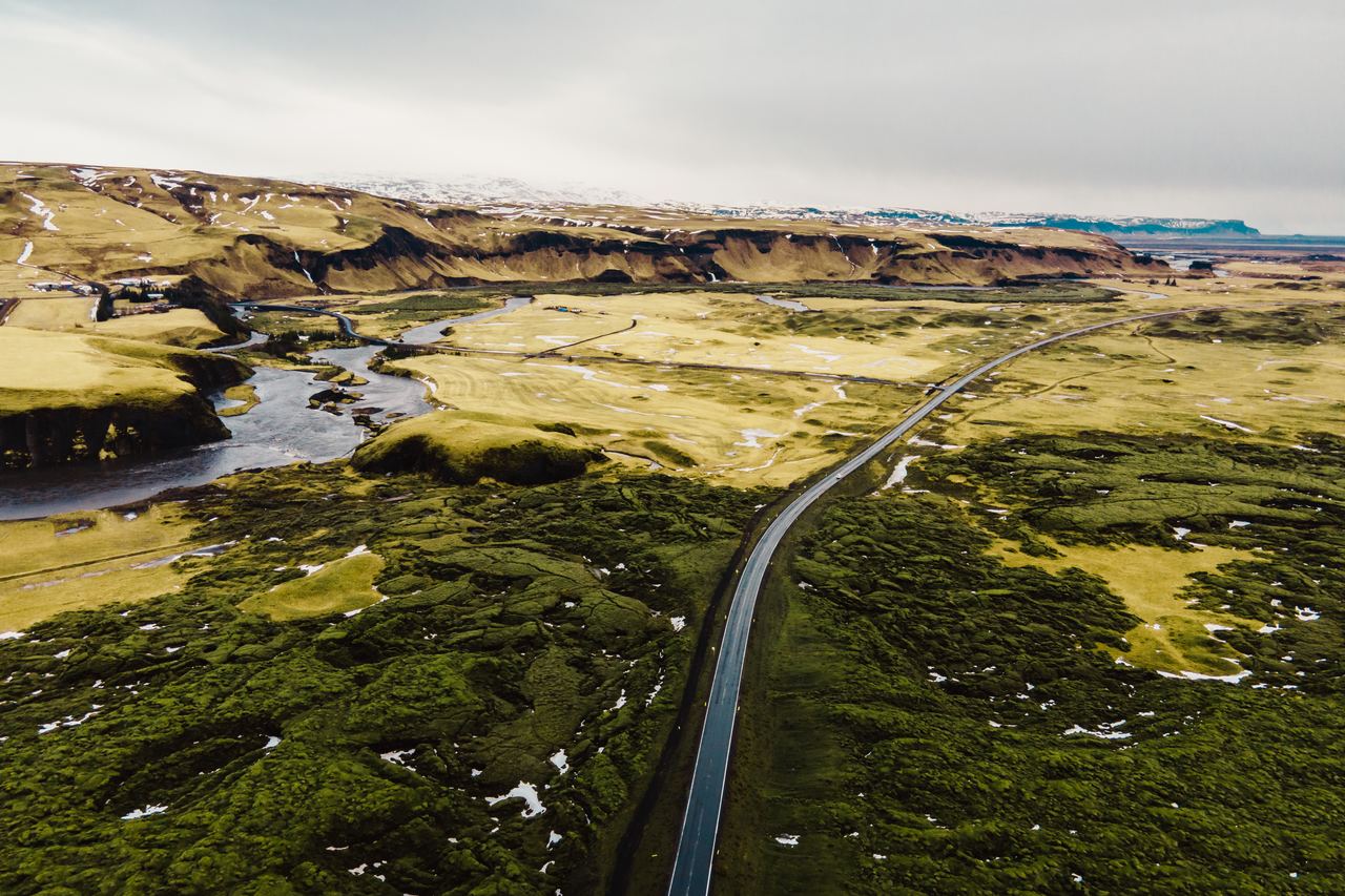 Aerial view of a green moss-covered lava field in Iceland with a single road running through it