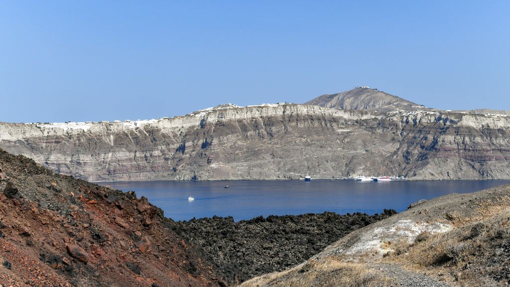 The dark lava island of Nea Kameni surrounded by the blue water of the Santorini caldera
