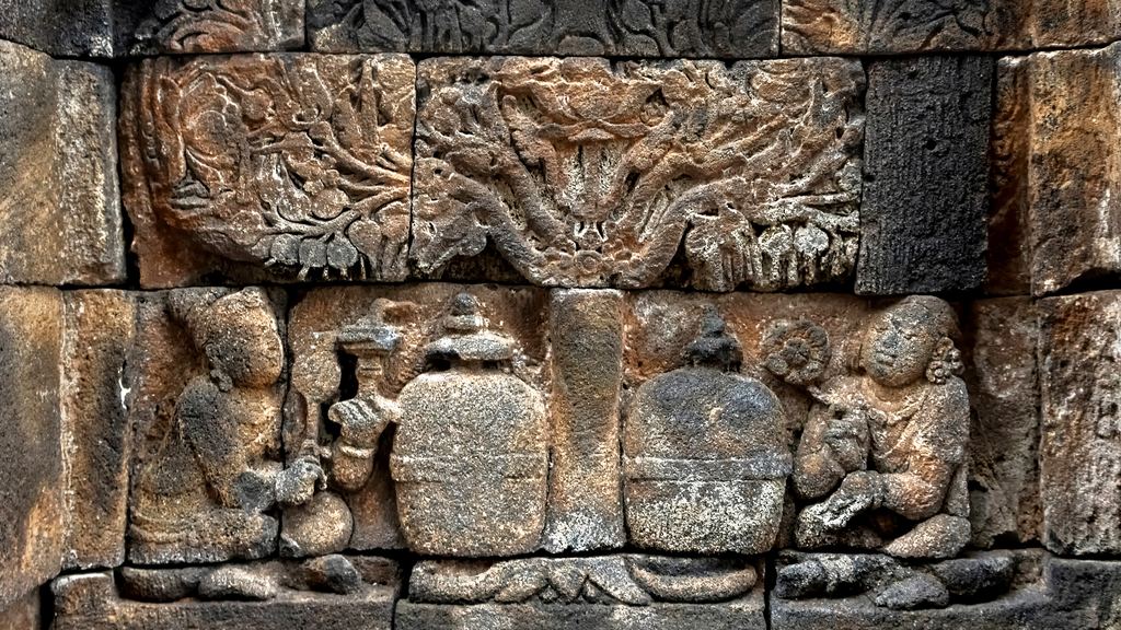 Carved stone relief panels and a seated Buddha on the walled galleries of Borobudur temple