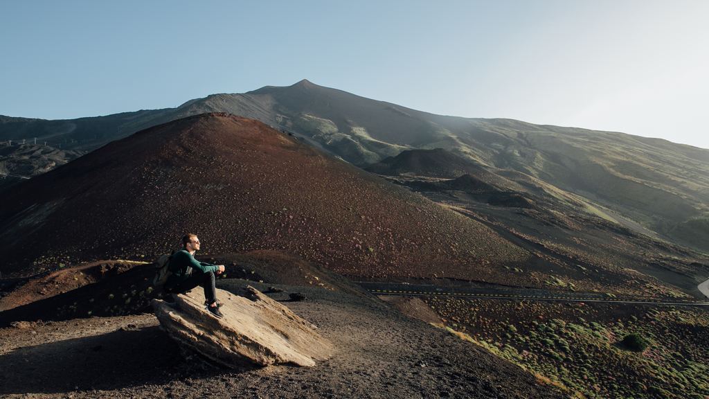 A walker resting on lava rock on the middle slopes of Mount Etna