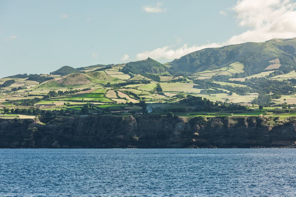 The coastline of São Miguel island in the Azores seen from the water, with green slopes rising from the Atlantic