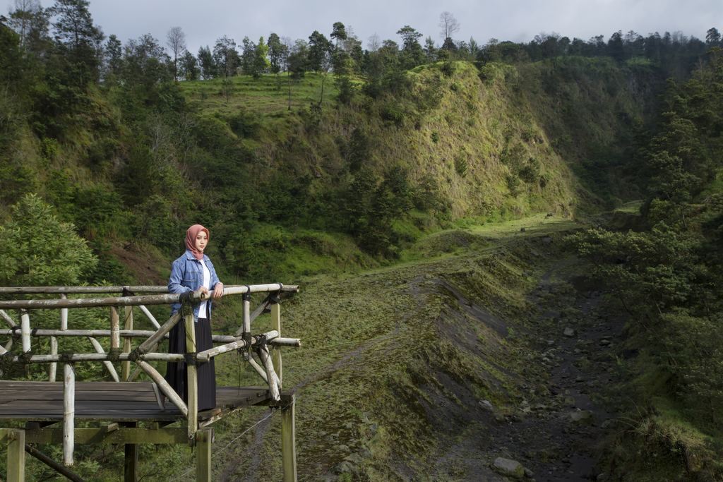 A visitor at the bamboo rails of the Kali Talang viewpoint looking towards Mount Merapi, Yogyakarta region