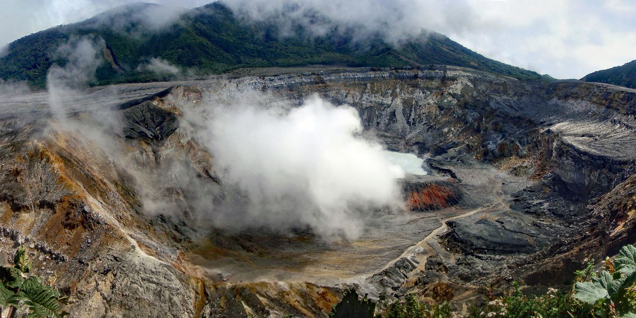 Panorama of the main crater of the Poás volcano in Costa Rica, with its pale acid lake and steaming grey walls