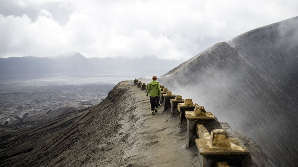 A visitor walking on the narrow crater rim of Mount Bromo above the Tengger sand sea