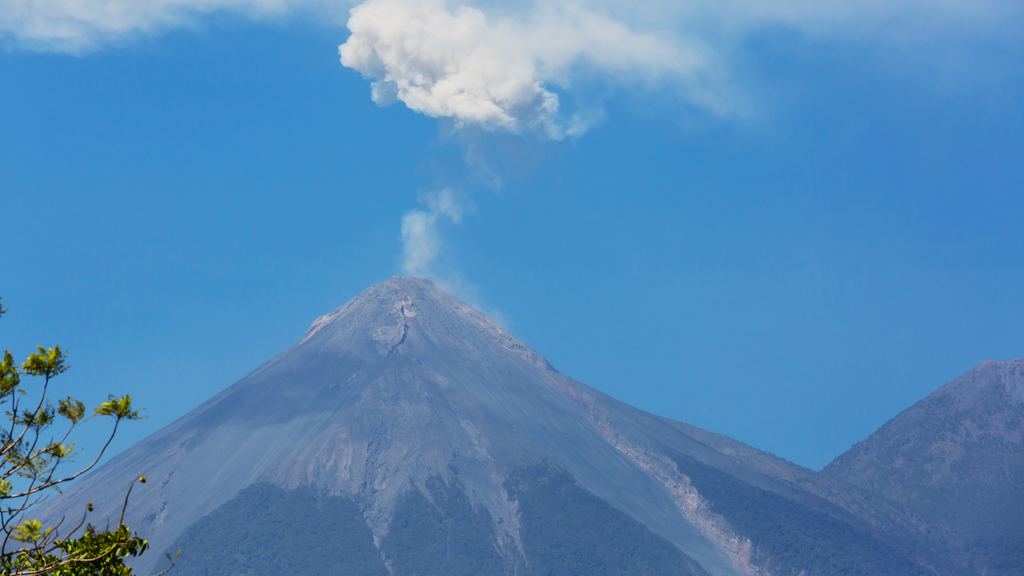 An ash plume rising from the summit of the Fuego volcano against a clear blue sky