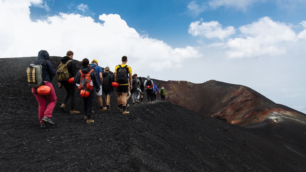A guided group walking across black volcanic scoria near the summit of Mount Etna